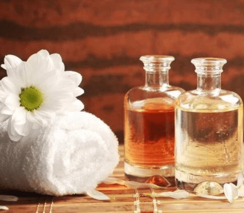 the 2 oil bottles on the wooden table with white color towel